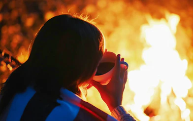 Girl enjoying warm drink by bonfire during Tromso Northern Lights tour.