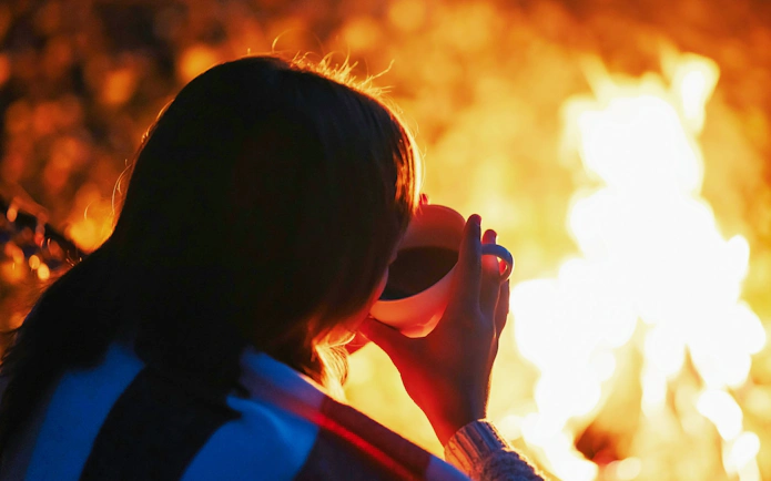 Girl enjoying warm drink by bonfire during Tromso Northern Lights tour.