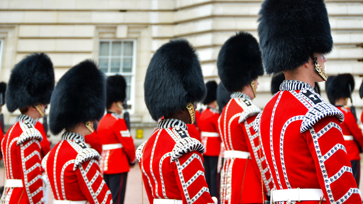 Guards in red uniforms and bearskin hats at Buckingham Palace ceremony.