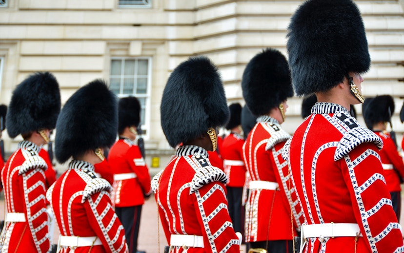 Guards in red uniforms and bearskin hats at Buckingham Palace ceremony.