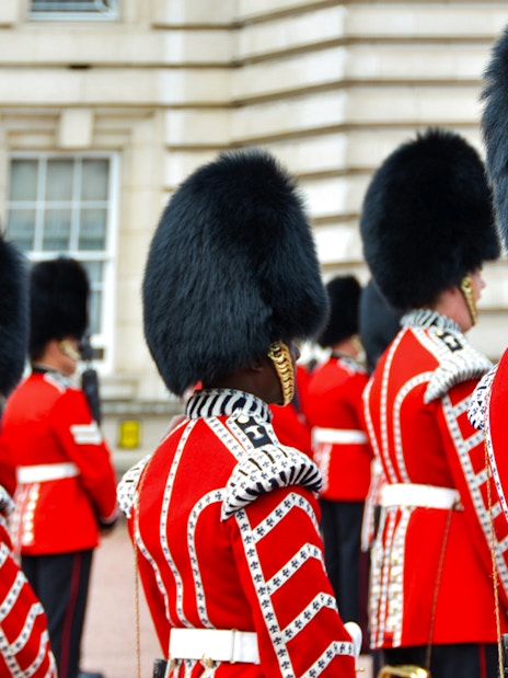 Guards in red uniforms and bearskin hats at Buckingham Palace ceremony.