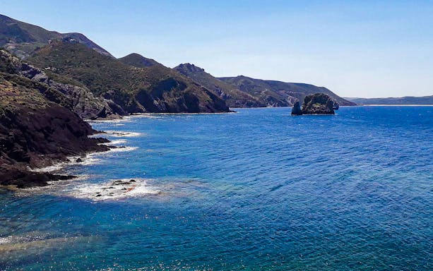 Faraglioni rock formations in blue sea along Nebida coastline during guided trek.