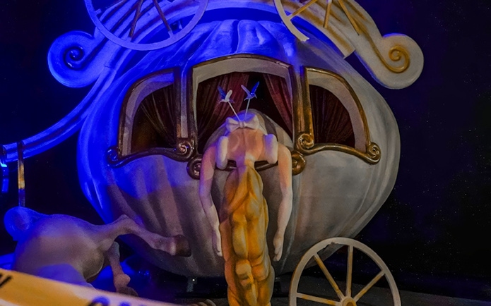 Surreal sculpture of a headless figure in front of a whimsical carriage at Banksy Limitless exhibit.