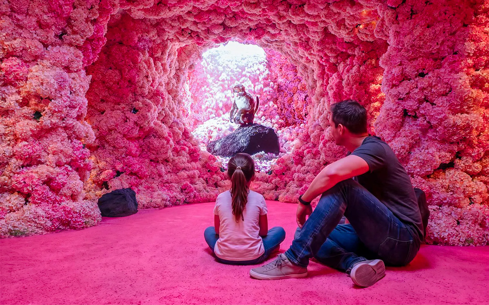 Visitors observing a monkey sculpture inside a pink floral cave at Mercer Labs Museum of Art.