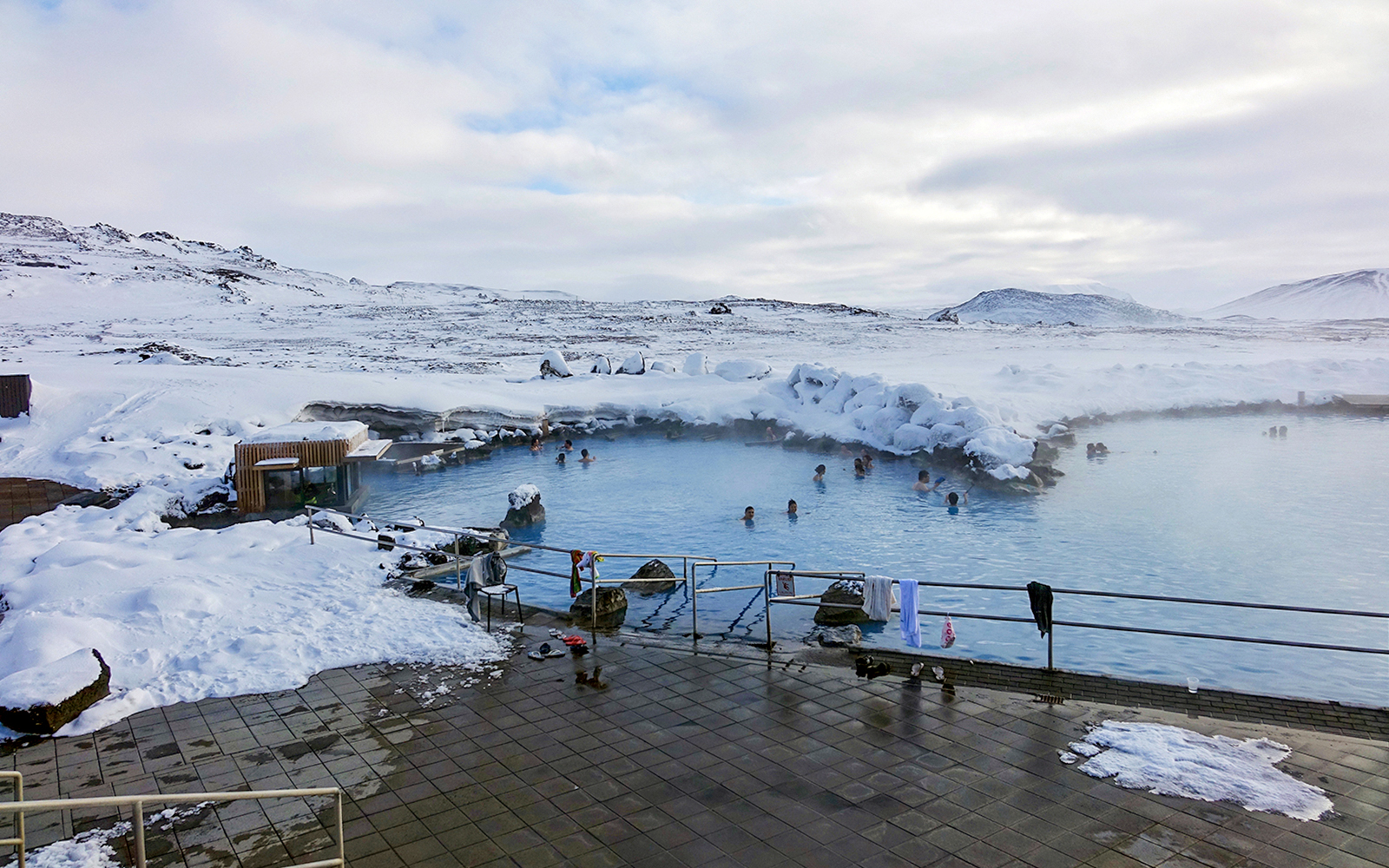 Guests relaxing in geothermal pool at Myvatn Nature Baths, Iceland, surrounded by snowy landscape.