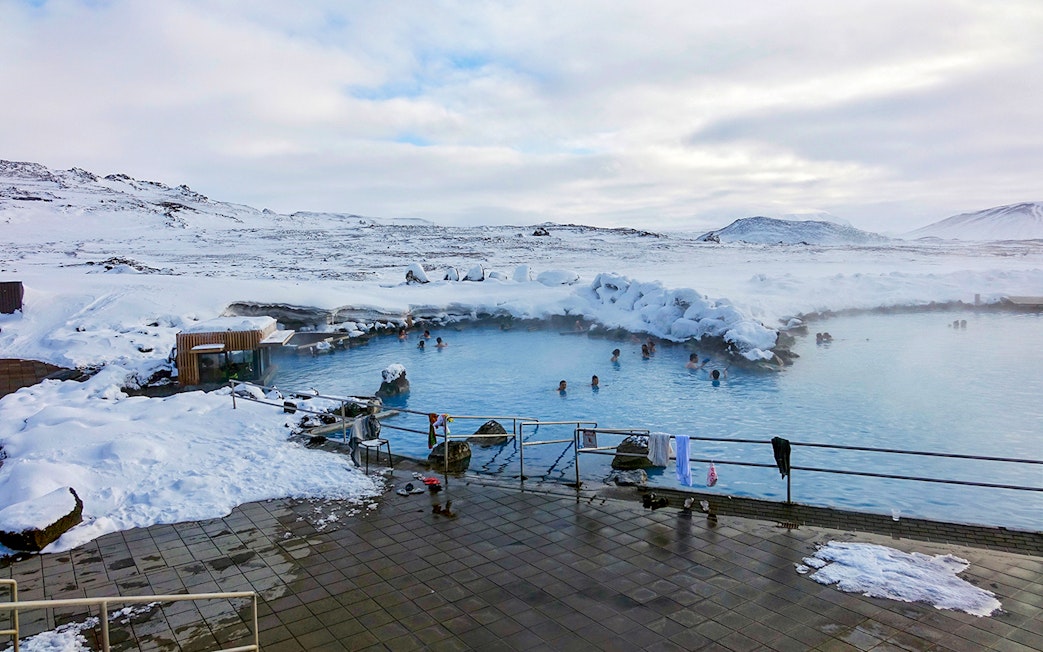 Guests relaxing in geothermal pool at Myvatn Nature Baths, Iceland, surrounded by snowy landscape.