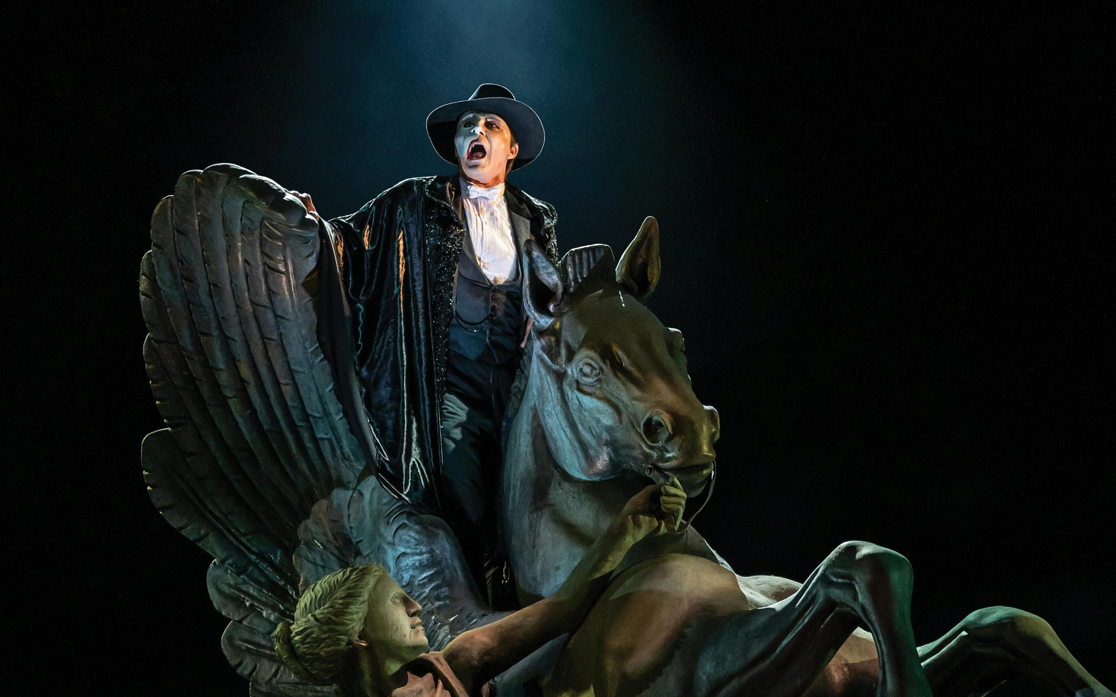 Performer in Phantom of the Opera costume on a winged horse statue.