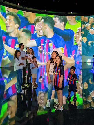 Visitors at Camp Nou viewing a large screen displaying FC Barcelona players celebrating.