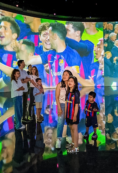 Visitors at Camp Nou viewing a large screen displaying FC Barcelona players celebrating.