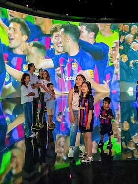 Visitors at Camp Nou viewing a large screen displaying FC Barcelona players celebrating.
