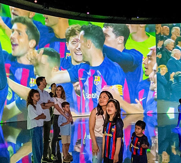 Visitors at Camp Nou viewing a large screen displaying FC Barcelona players celebrating.