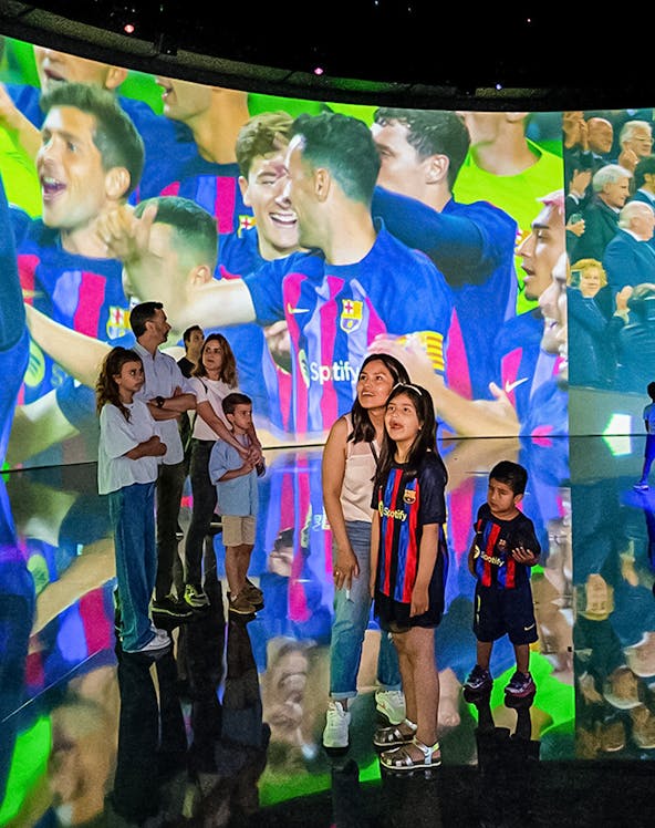 Visitors at Camp Nou viewing a large screen displaying FC Barcelona players celebrating.
