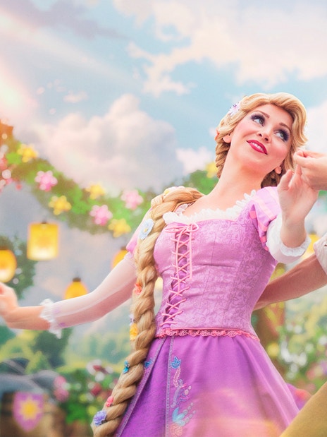 Rapunzel and Flynn dancing at Disneyland Paris with lanterns and floral backdrop.