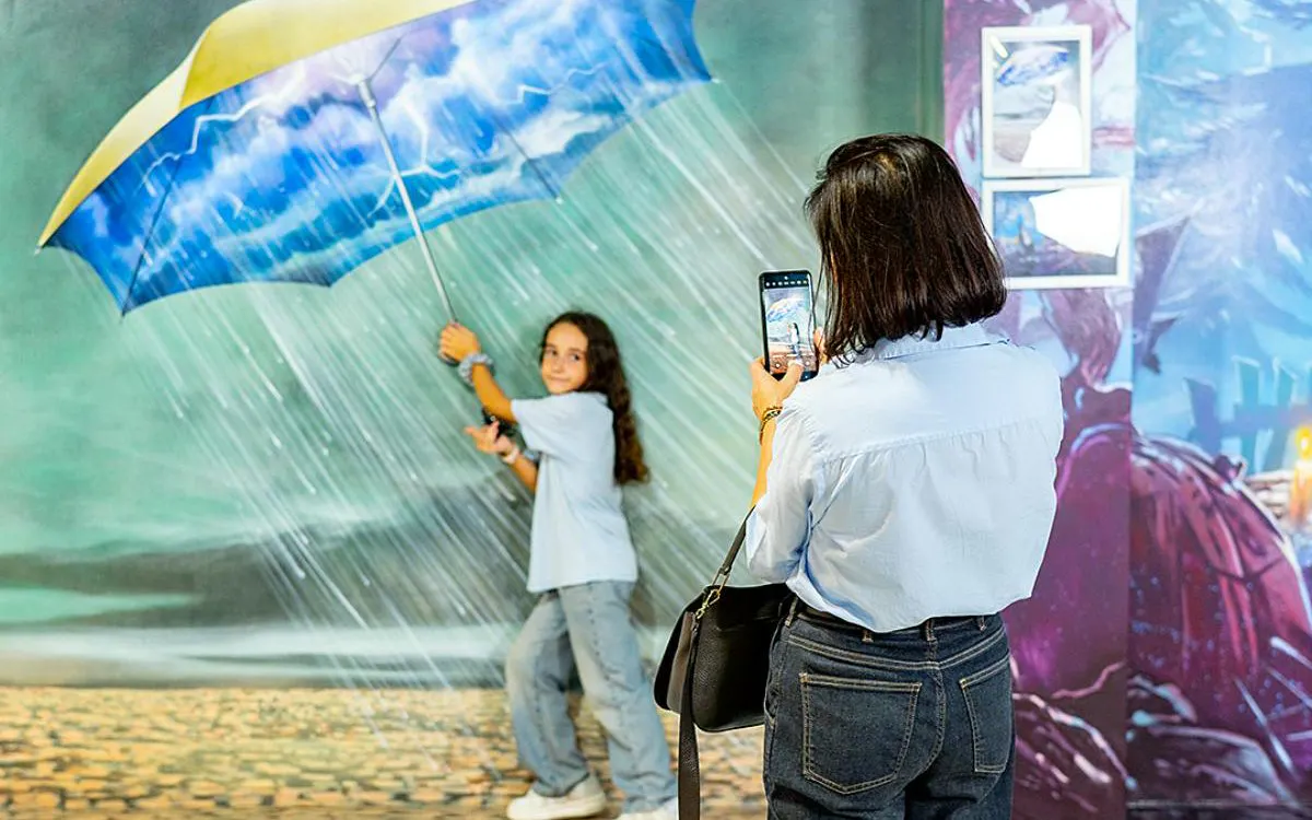 Child posing with umbrella in rain illusion at Big Fun Museum, Barcelona.