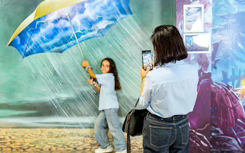 Child posing with umbrella in rain illusion at Big Fun Museum, Barcelona.