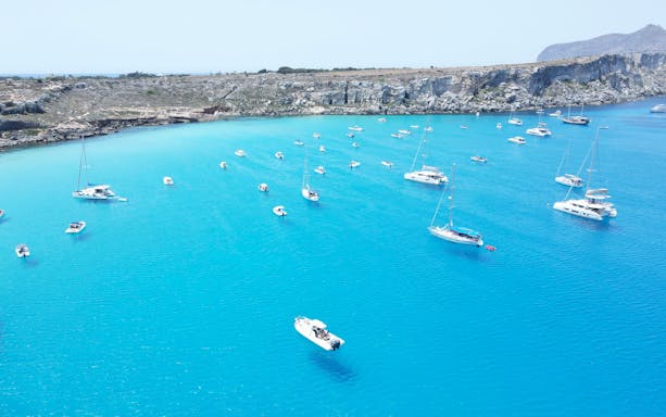 Boat tours in clear blue waters near rocky coastline of Favignana and Levanzo.