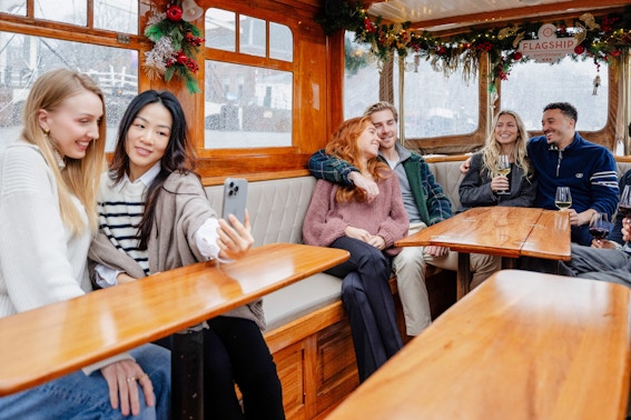 Guests enjoying an evening canal cruise in Amsterdam, passing illuminated bridges and historic buildings in winter.