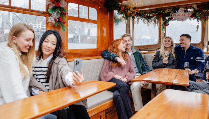 Guests enjoying an evening canal cruise in Amsterdam, passing illuminated bridges and historic buildings in winter.