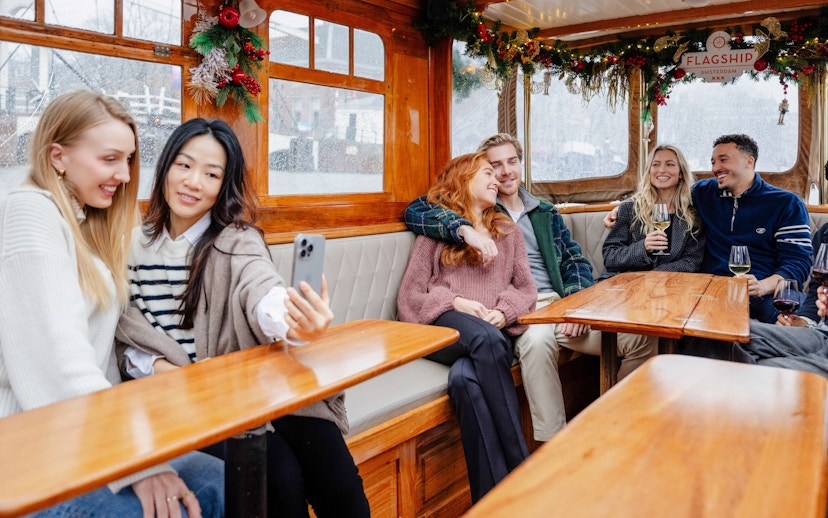 Guests enjoying an evening canal cruise in Amsterdam, passing illuminated bridges and historic buildings in winter.
