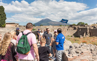 Tour group exploring Pompeii ruins with Mount Vesuvius in the background.