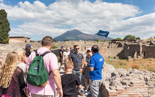 Tour group exploring Pompeii ruins with Mount Vesuvius in the background.