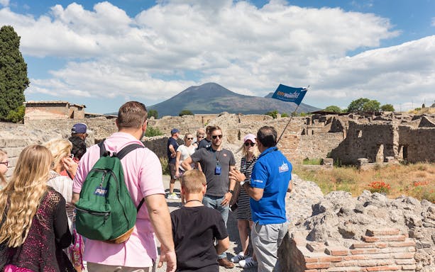 Tour group exploring Pompeii ruins with Mount Vesuvius in the background.