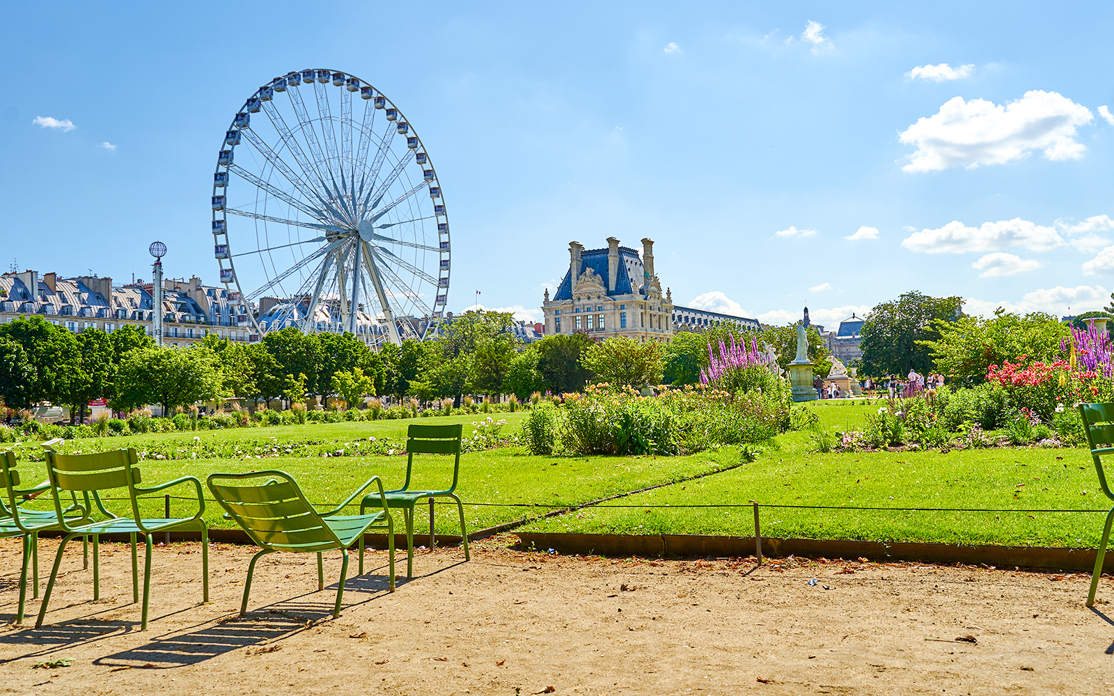 Ferris wheel and chairs in Tuileries Garden, Paris, with Louvre in background.