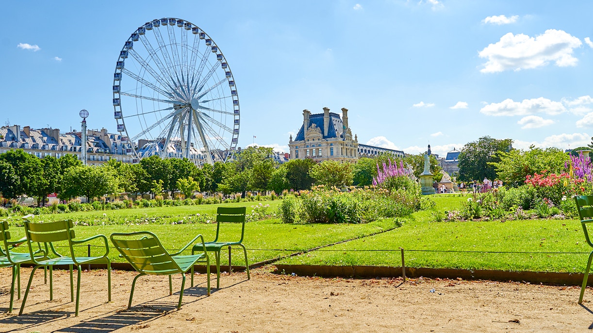 Ferris wheel and chairs in Tuileries Garden, Paris, with Louvre in background.