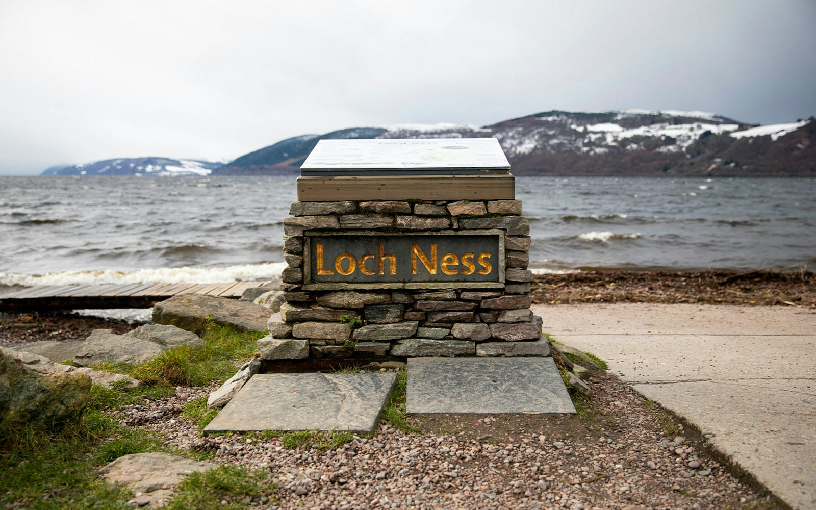Loch Ness sign with view of the lake and snow-capped hills from Dores Beach.
