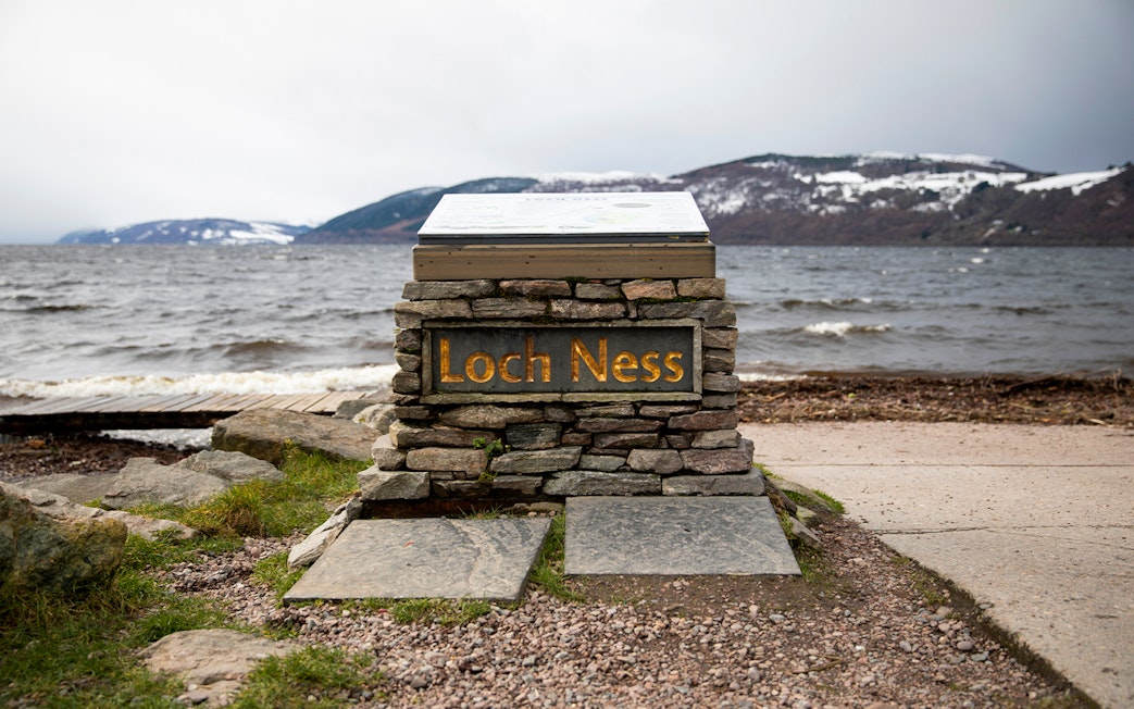 Loch Ness sign with view of the lake and snow-capped hills from Dores Beach.