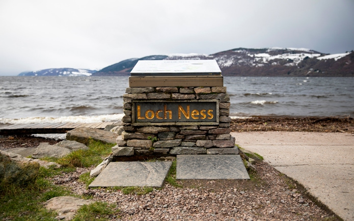 Loch Ness sign with view of the lake and snow-capped hills from Dores Beach.