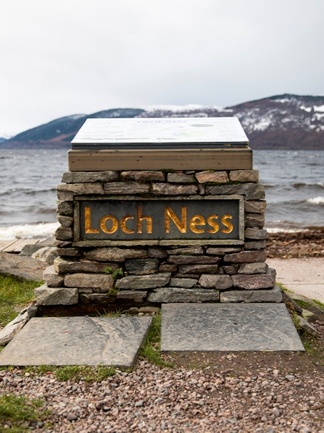 Loch Ness sign with view of the lake and snow-capped hills from Dores Beach.
