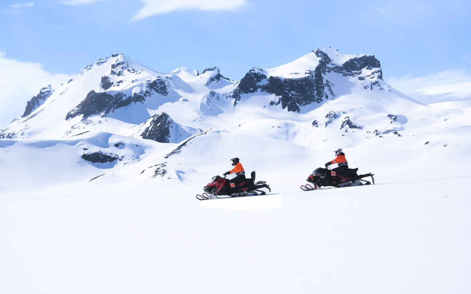 Snowmobilers on Langjökull Glacier with snowy mountain backdrop.