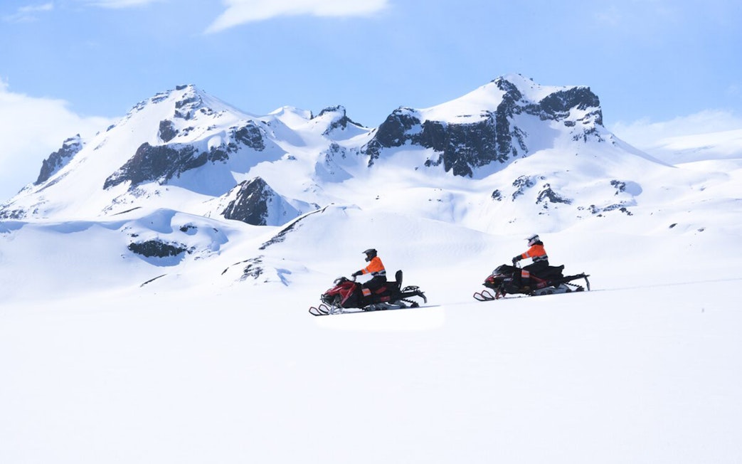 Snowmobilers on Langjökull Glacier with snowy mountain backdrop.