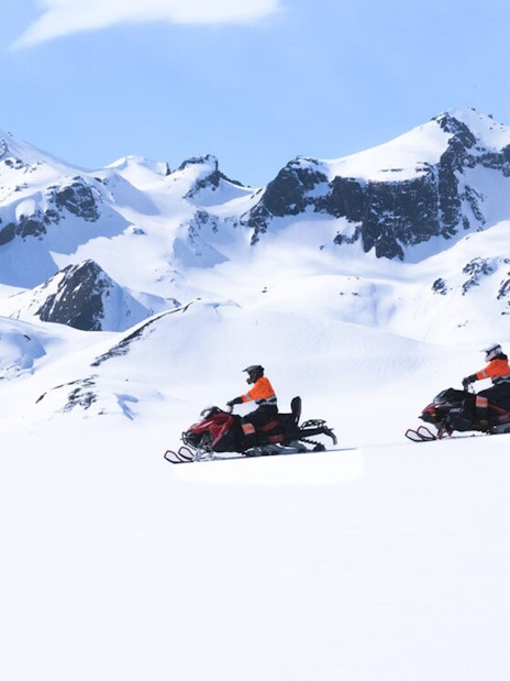 Snowmobilers on Langjökull Glacier with snowy mountain backdrop.