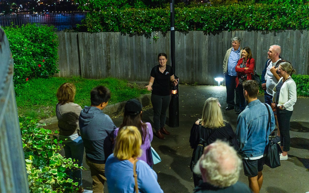 Group listening to guide during Sydney True Crime Stories tour at night.