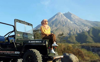 Jeep tour at sunrise near Mount Merapi, Indonesia, with a person seated on the vehicle.
