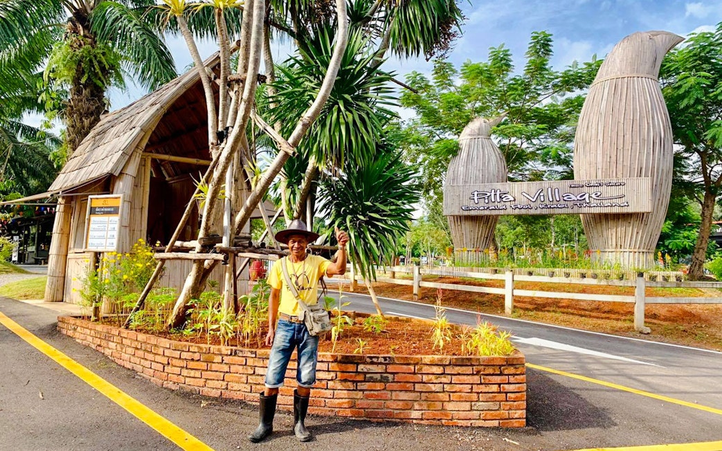 Entrance to Pita Village with a local guide standing near tropical plants.