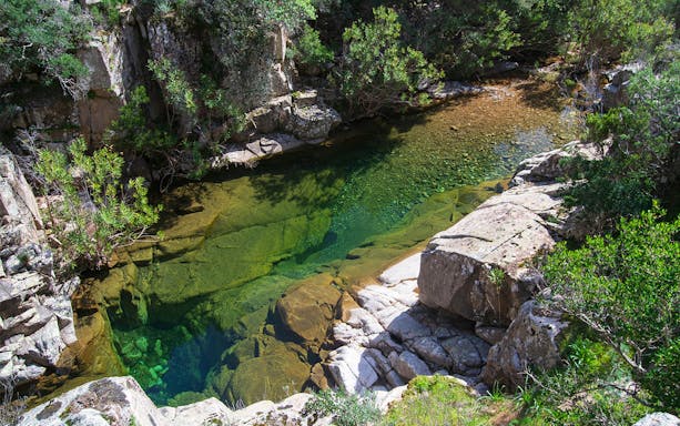 Trekker crossing rocky terrain towards Piscina Irgas Waterfall in Villacidro, Sardinia.