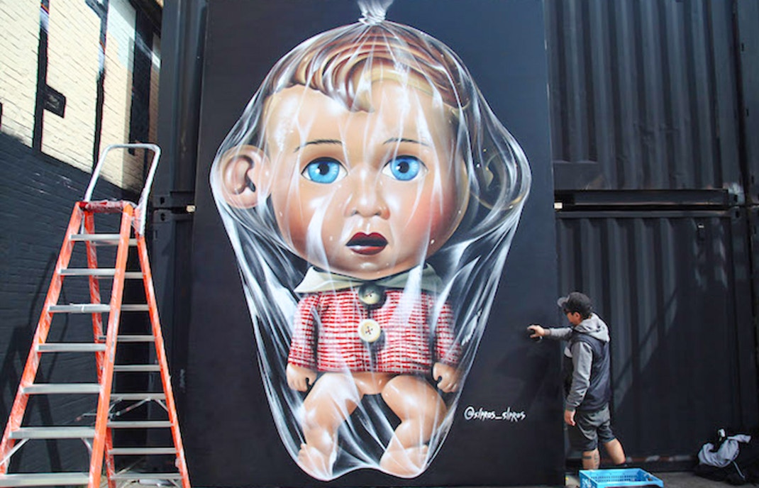 Street art mural of The Big Ears Old School Doll by Sipros, featuring a large doll wrapped in plastic.
