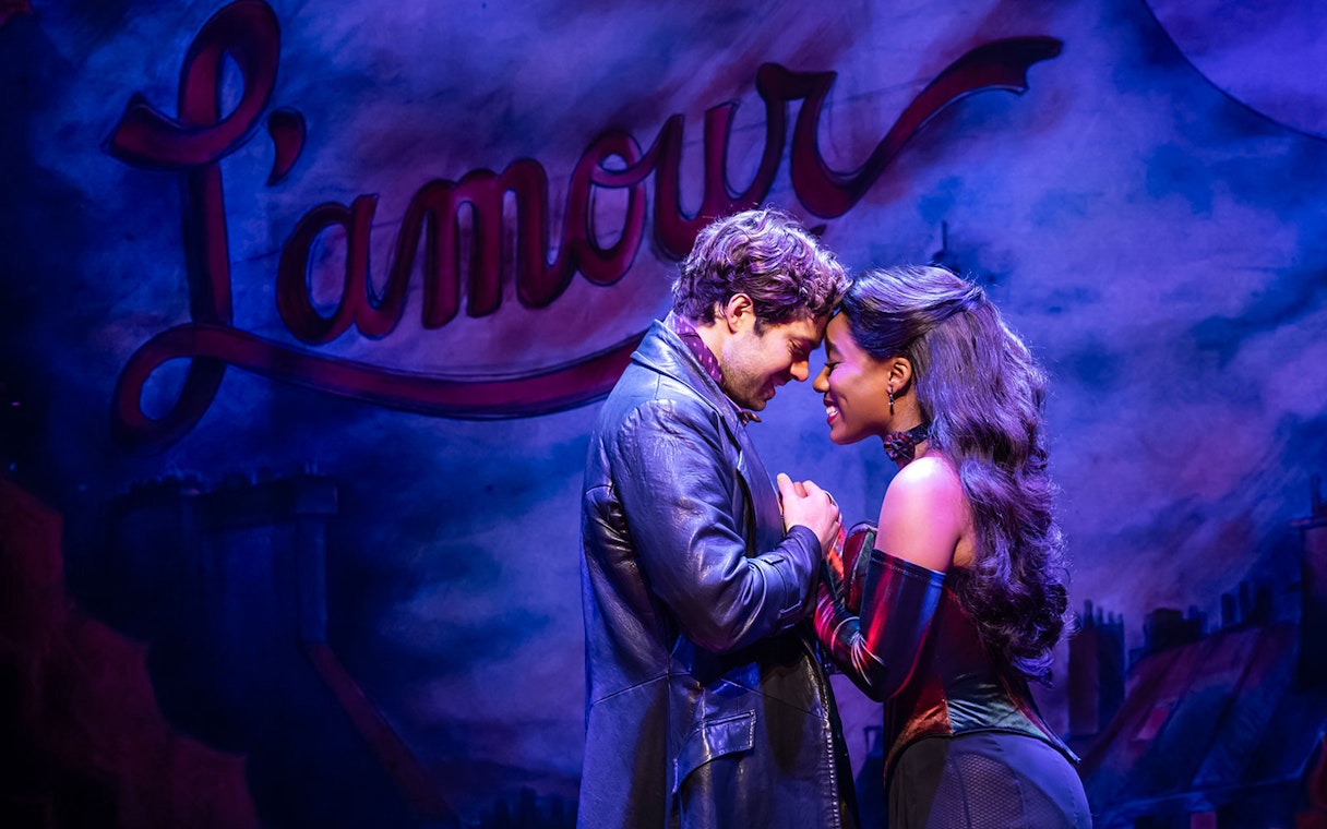 Actors embrace on stage during Moulin Rouge! The Musical with "L'amour" in the background.