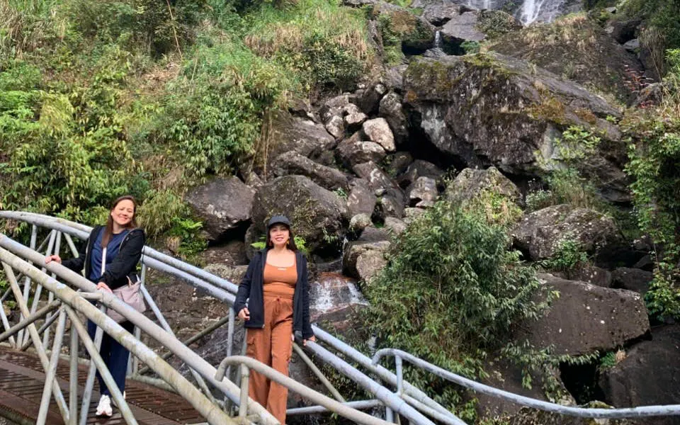 Two people on a bridge in Sapa, Vietnam, with a rocky waterfall backdrop.