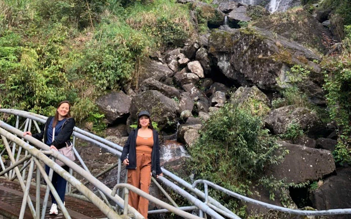 Two people on a bridge in Sapa, Vietnam, with a rocky waterfall backdrop.