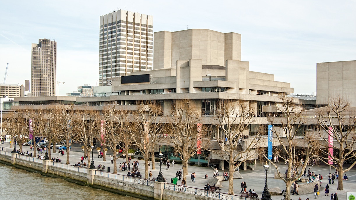 National Theatre on South Bank, London with people walking along the riverside.