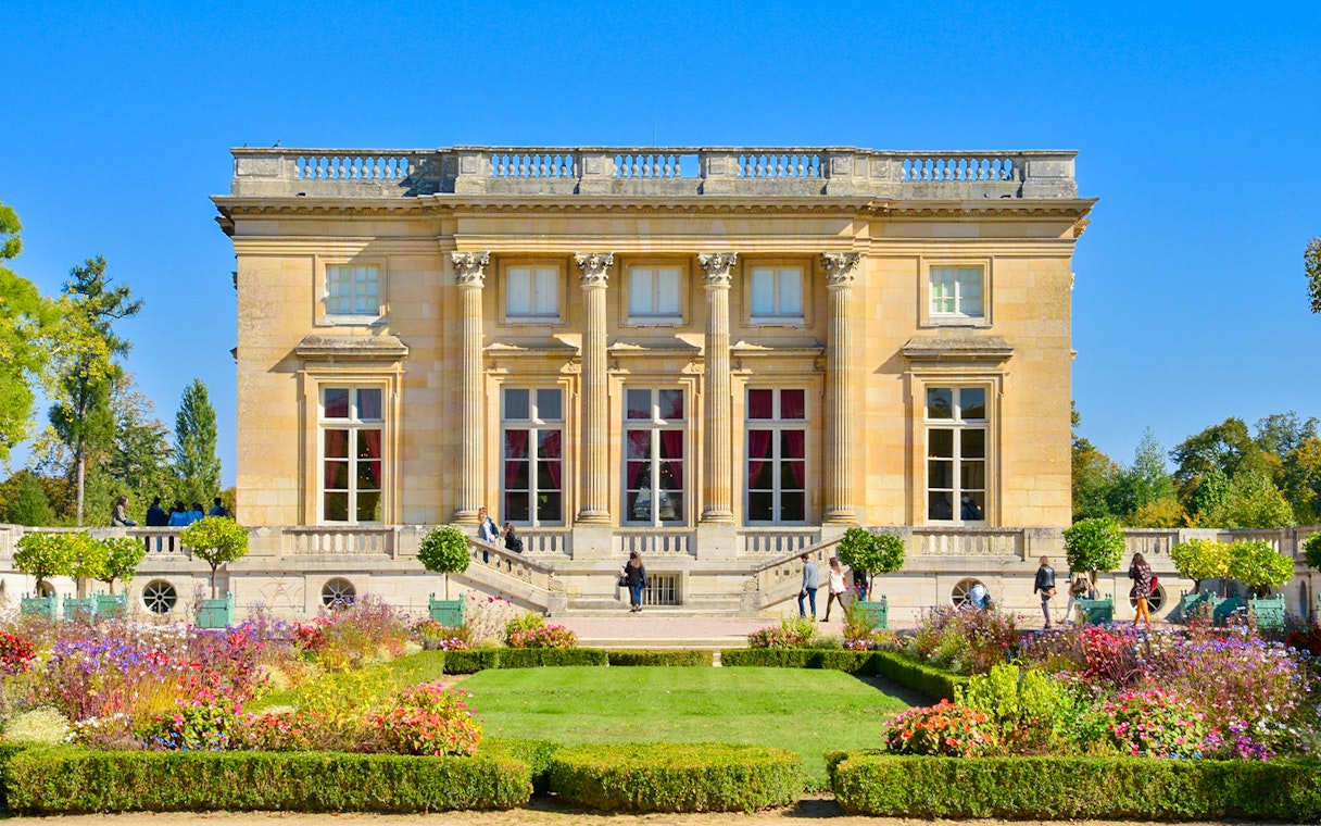 Trianon Palace with gardens and visitors in Versailles, France.