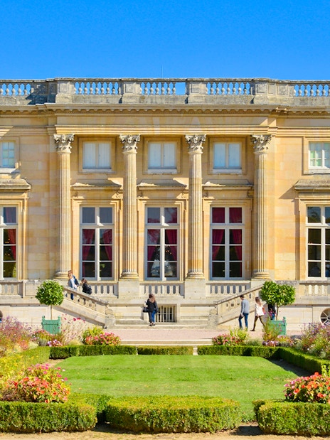 Trianon Palace with gardens and visitors in Versailles, France.