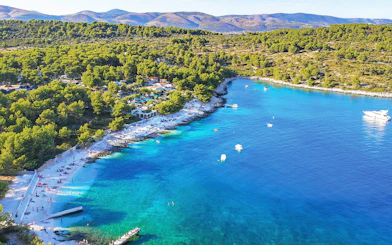 Aerial view of Duga Bay with turquoise waters, boats, and a forested coastline.