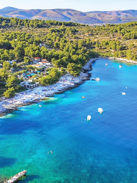 Aerial view of Duga Bay with turquoise waters, boats, and a forested coastline.