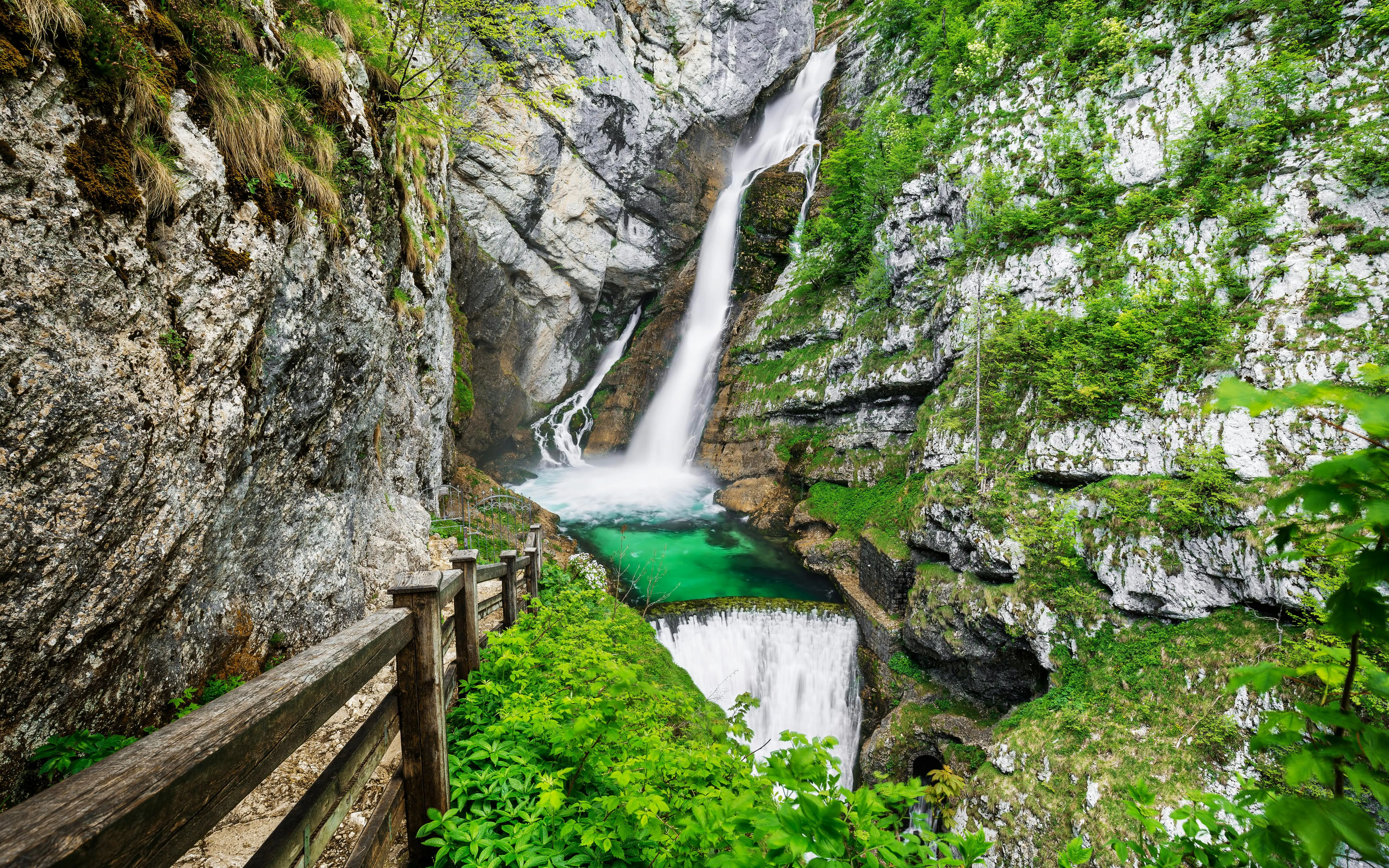 Savica Waterfall cascading into a turquoise pool, surrounded by lush greenery and rocky cliffs in Slovenia.