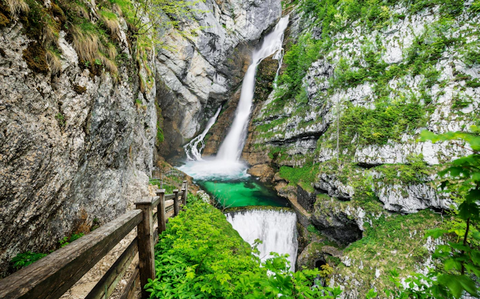 Savica Waterfall cascading into a turquoise pool, surrounded by lush greenery and rocky cliffs in Slovenia.